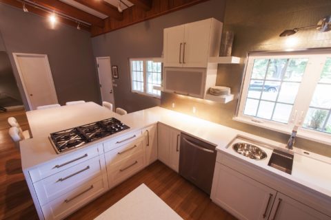 Tulsa kitchen remodel featuring a white kitchen peninsula with a gas cooktop, a seating space, open shelves, a Galley Workstation kitchen sink, and a stainless steel dishwasher.