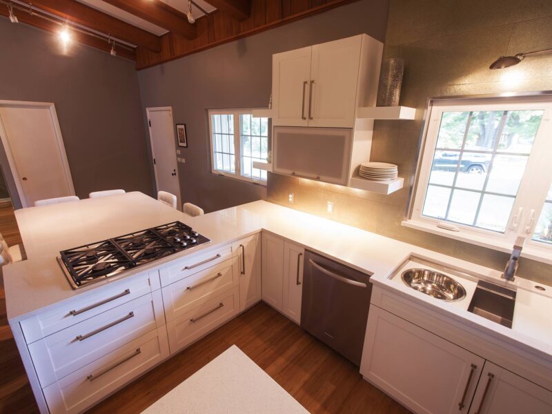 Tulsa kitchen remodel featuring a white kitchen peninsula with a gas cooktop, a seating space, open shelves, a Galley Workstation kitchen sink, and a stainless steel dishwasher.