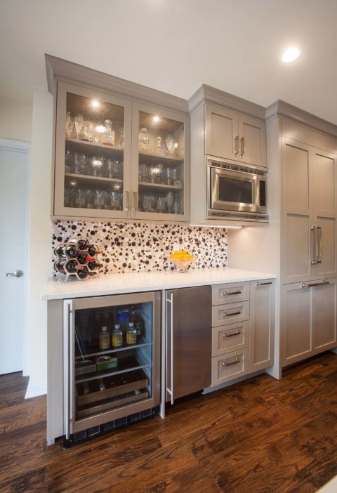 Tulsa kitchen remodel featuring a kitchen beverage drawer space with a microwave, an undercounter refrigerator, an ice maker, wall cabinets with beaded glass doors, a paneled refrigerator and freezer, and wood floors.