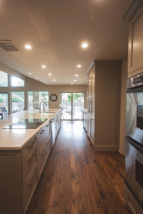 Tulsa kitchen remodel featuring a large kitchen island with a Galley Workstation kitchen sink, an induction cooktop, a stainless steel dishwasher, double ovens, and wood flooring.