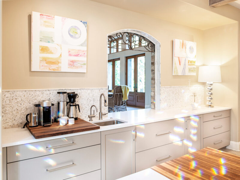 Tulsa kitchen remodel featuring a coffee and beverage space with a bar sink, base cabinet storage, a countertop, and a height-arched living room pass-through with a backsplash.