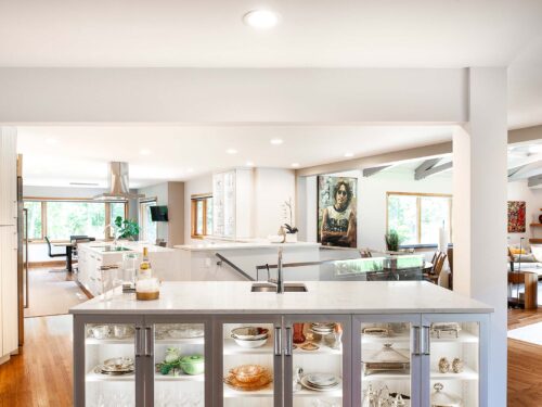 Tulsa kitchen remodel featuring an island with cabinet storage, a bar sink, and a lit, glass-front bar. The kitchen includes white countertops, wood floors, and Bosch professional stainless steel appliances.