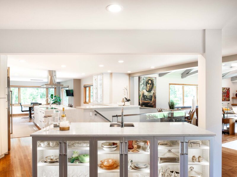 Tulsa kitchen remodel featuring an island with cabinet storage, a bar sink, and a lit, glass-front bar. The kitchen includes white countertops, wood floors, and Bosch professional stainless steel appliances.