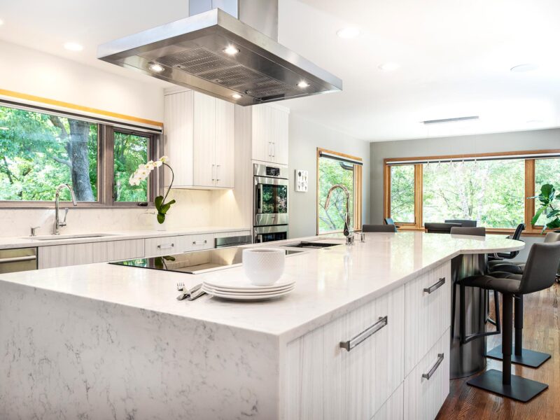 Tulsa kitchen remodel featuring a stainless steel Bosch professional vent hood, a large island with a waterfall counter edge, a Bosch induction cooktop, a Galley Workstation, seating space, and marble counters.