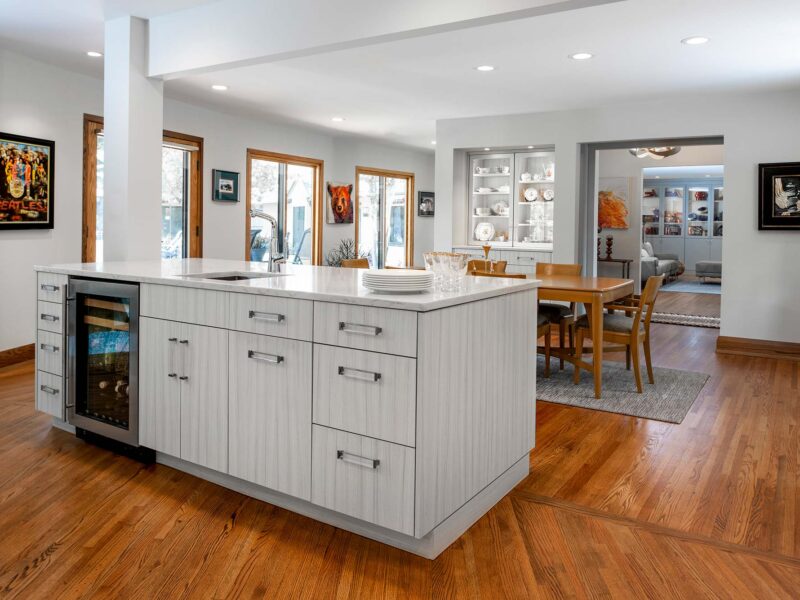 Tulsa kitchen remodel featuring white cabinet storage, a marble countertop, and Bosch appliances. The bar island includes storage, a sink, and a Bosch wine and beverage refrigerator, all on wood floors.