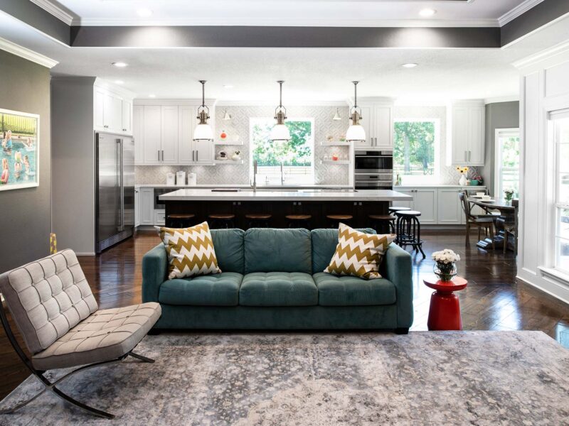 South Tulsa kitchen remodel featuring an open-concept kitchen and living room, a large island with seating, a Galley Workstation, an induction cooktop, stainless steel appliances, a decorative tile backsplash, a clean-up sink, and open shelves.