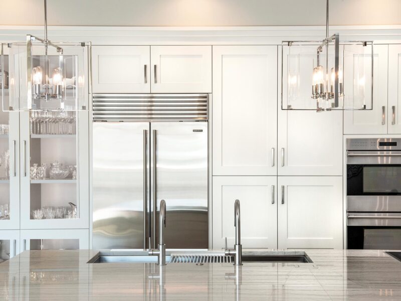 Tulsa kitchen remodel featuring a white tall pantry storage unit, a stainless steel Sub-Zero refrigerator and freezer, Wolf double ovens, a large island with pendant lights, a Galley Workstation, and a Wolf gas cooktop.