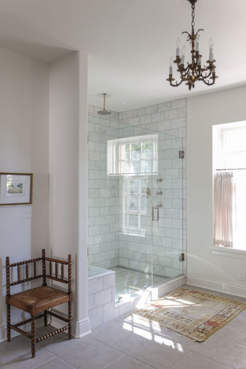 A spacious Tulsa master bathroom remodel featuring a large shower with a rainfall shower head, a glass door with a curb, subway tile, and a decorative pendant light.