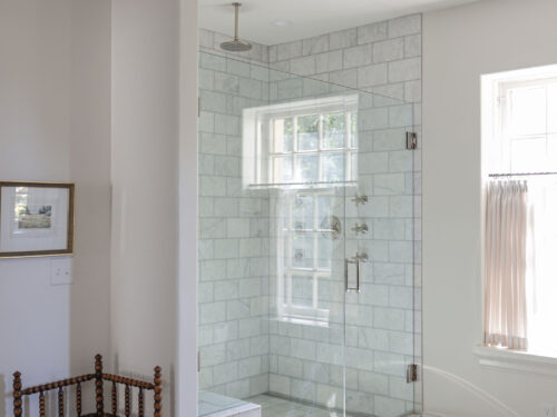 A spacious Tulsa master bathroom remodel featuring a large shower with a rainfall shower head, a glass door with a curb, subway tile, and a decorative pendant light.