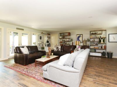 Open concept living room remodel with seating, decorative open shelving, and brown wood plank flooring. Tulsa living room design.
