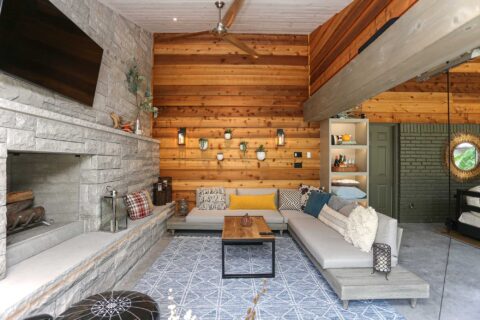 Spacious open-concept patio featuring stone wood-burning fireplace, comfortable lounge seating, and wall-mounted television in Tulsa design and remodel.