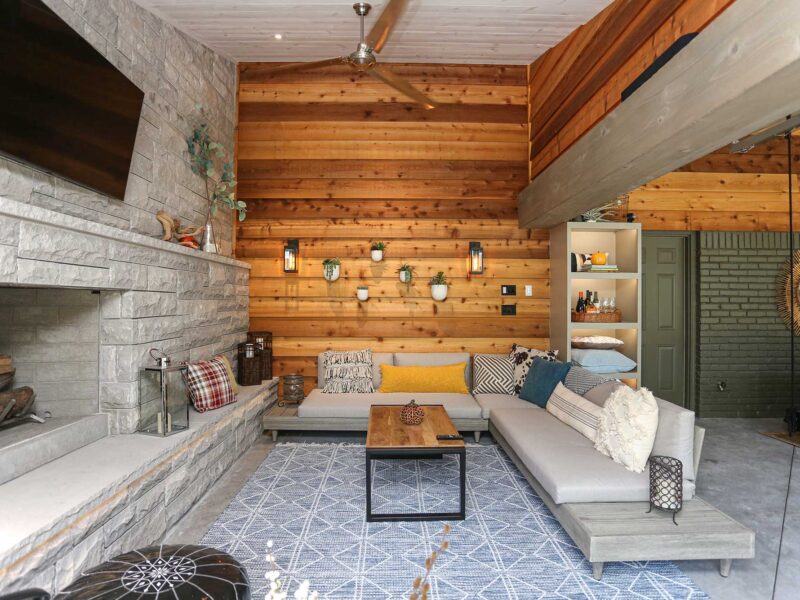 Spacious open-concept patio featuring stone wood-burning fireplace, comfortable lounge seating, and wall-mounted television in Tulsa design and remodel.