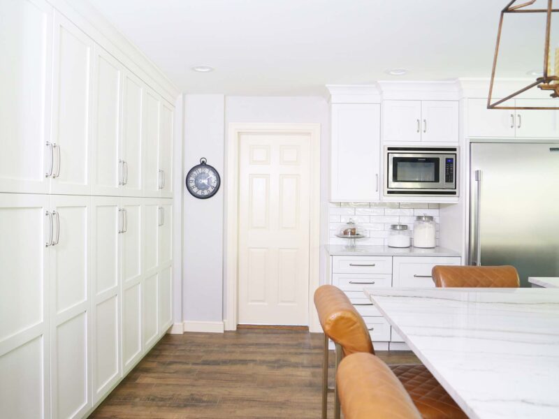 Tulsa kitchen design featuring a white cabinet tall pantry storage unit, a Frigidaire microwave, a Sub-Zero stainless steel refrigerator and freezer, wood flooring, and island seating space.