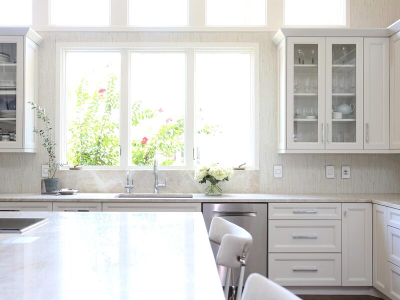 Tulsa kitchen remodel featuring base and wall cabinet storage with glass door fronts, a clean-up sink, a stainless steel dishwasher, a decorative tile backsplash, and a large island with seating.