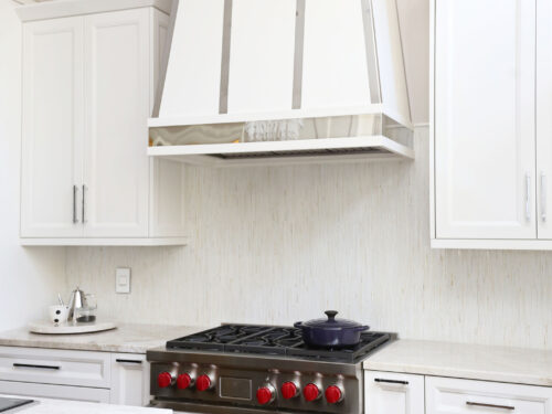 Tulsa kitchen design and remodel featuring a Wolf range, a decorative hood, a tile backsplash, and extensive white base and wall cabinet storage.