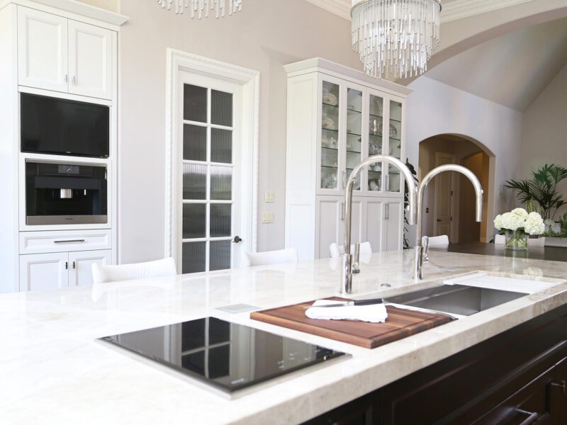 Tulsa kitchen remodel featuring a large island with a Galley Workstation, tap faucets, a Wolf induction cooktop, a Miele coffee center, and tall white storage cabinets.