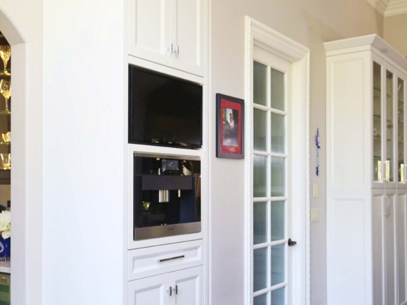 Tulsa kitchen remodel featuring a Miele tall coffee center, a TV, white storage cabinets, and refinished wood floors.