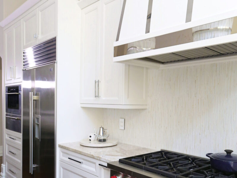 Tulsa kitchen design and remodel featuring a Sub-Zero refrigerator, a Wolf range, a decorative hood, a tile backsplash, and extensive white base and wall cabinet storage.