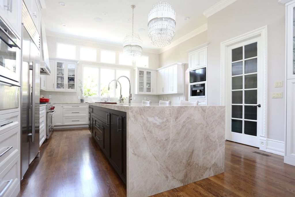 Timeless elegant large south Tulsa kitchen large island and rich brown cabinet storage accented by a waterfall edge counter top, wood floors, white perimeter cabinets and stainless appliances
