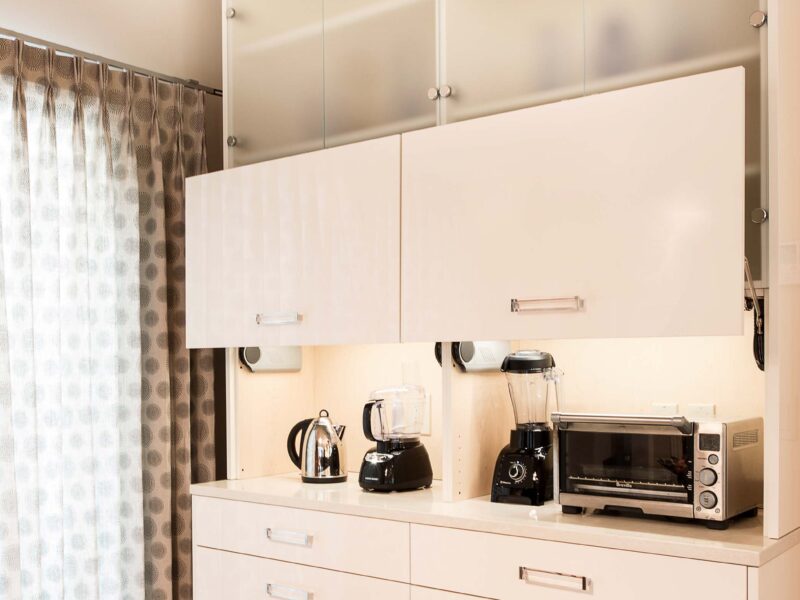 Kitchen coffee and beverage center with pull-up cabinet panels, frosted glass wall cabinet storage, and base drawer storage.