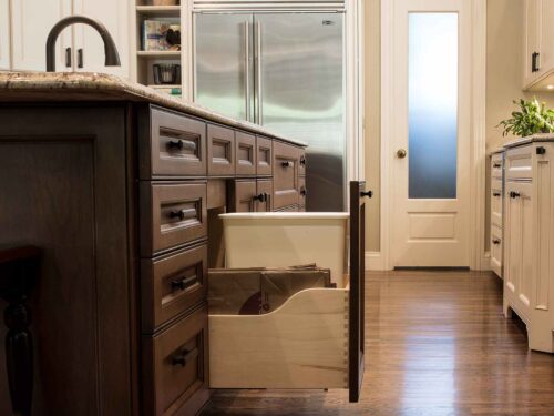 Tulsa kitchen remodel featuring a pullout trash, brown island drawer storage, cream base cabinet storage, wood flooring, and a Sub-Zero freezer and refrigerator.