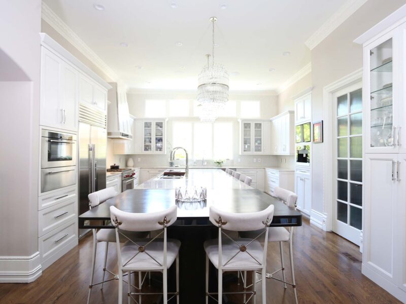 Tulsa kitchen design featuring a large island with a Galley Workstation, Sub-Zero and Wolf stainless steel appliances, and refinished wood floors. The space has brown cabinets, island chandeliers, and seating at a table.