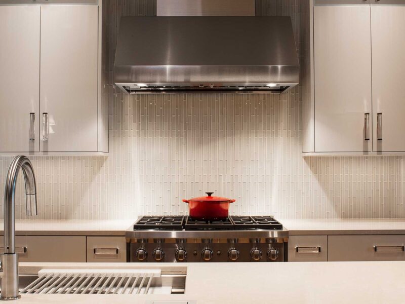 Tulsa kitchen remodel featuring a Wolf professional gas range with a vent hood for the cooking space, a ceramic tile backsplash, and white flat-panel cabinet storage.