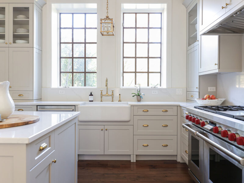 Tulsa kitchen remodel featuring a kitchen island with a gas range, bright cabinets, wood floors, a farmhouse sink, and gold hardware.
