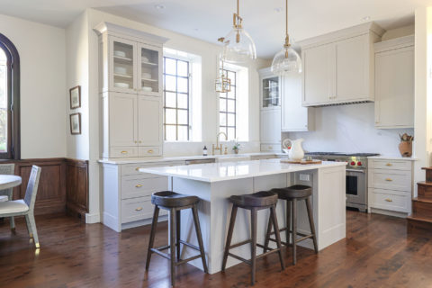 White kitchen design island and pendant lighting, farmhouse apron-sink, Wolf gas range, drawer storage with wood floors Tulsa kitchen remodel