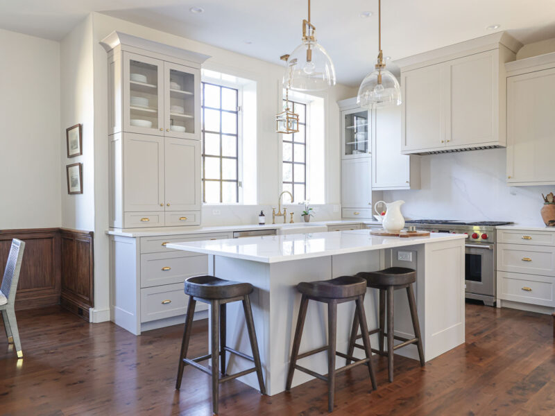Tulsa kitchen remodel featuring a white kitchen design with an island, pendant lighting, a farmhouse apron sink, a Wolf gas range, and built-in drawer storage, all on beautiful wood floors.