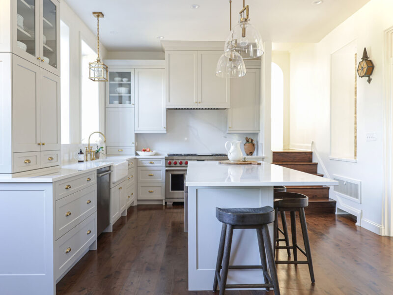 Tulsa kitchen designer showcasing a white kitchen remodel with an island, seating, and pendant lighting. The space features a farmhouse apron sink, a Wolf gas range, and built-in drawer and door storage.