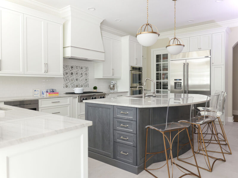 Tulsa kitchen design and remodel featuring a large kitchen island with cabinet storage, seating, and pendant lights. The space includes a range top, a decorative hood, JennAir and KitchenAid appliances, and an arched opening.