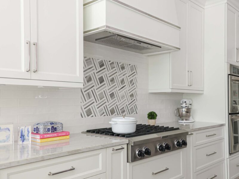 Tulsa kitchen design and remodel featuring a KitchenAid range top, a decorative vent hood, and a tile backsplash, with ample cabinet storage.