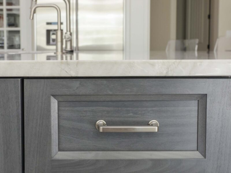 Tulsa kitchen remodel featuring gray cabinet drawer storage, a white countertop, a kitchen island, and a stainless steel refrigerator.