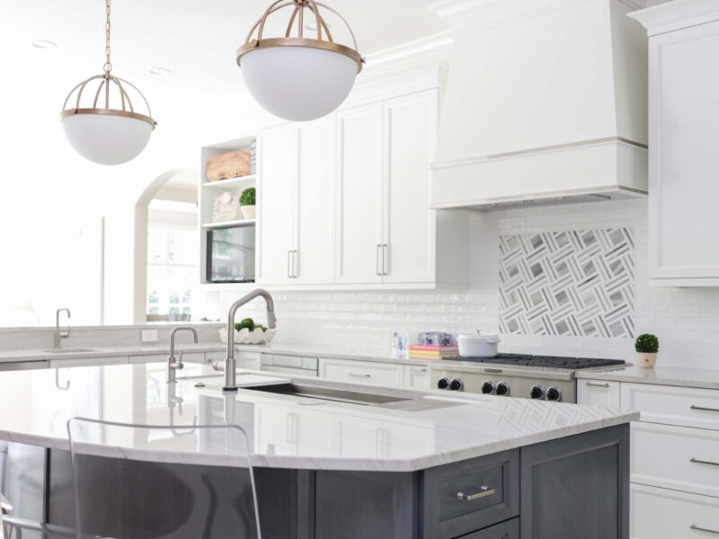 Tulsa kitchen remodel featuring a large white kitchen island with seating and an undermount sink. The space includes a range top, a decorative vent hood, and pendants over the island.