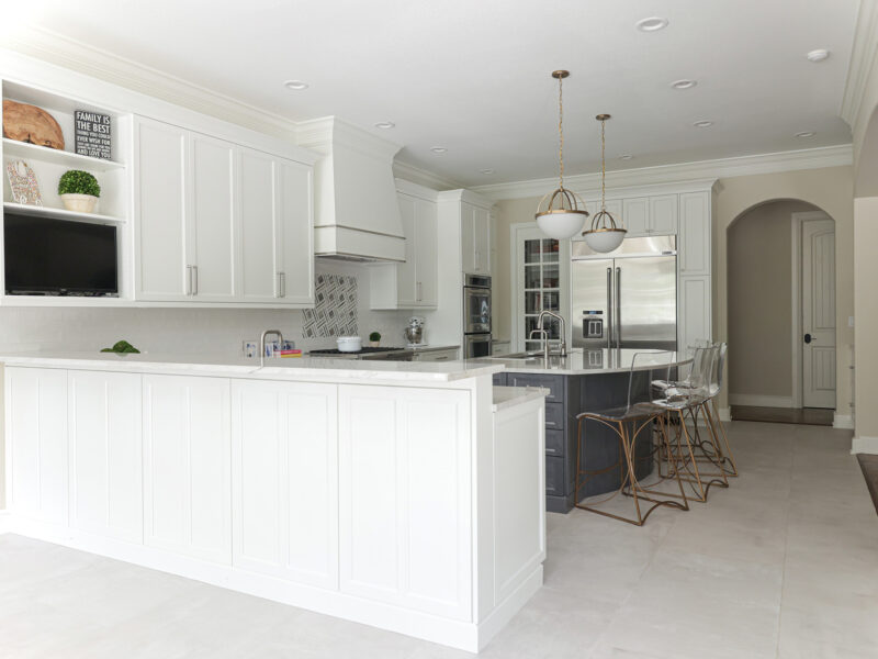 Tulsa kitchen design and remodel featuring a peninsula, a large island with seating, a decorative hood over a rangetop, and JennAir and KitchenAid appliances. The space also includes an arched opening and pendant lights.