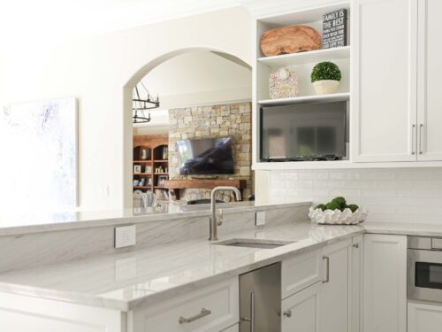 Tulsa kitchen remodel featuring a white kitchen peninsula with an under counter ice maker, a bar sink, a subway tile backsplash, and large crown molding.