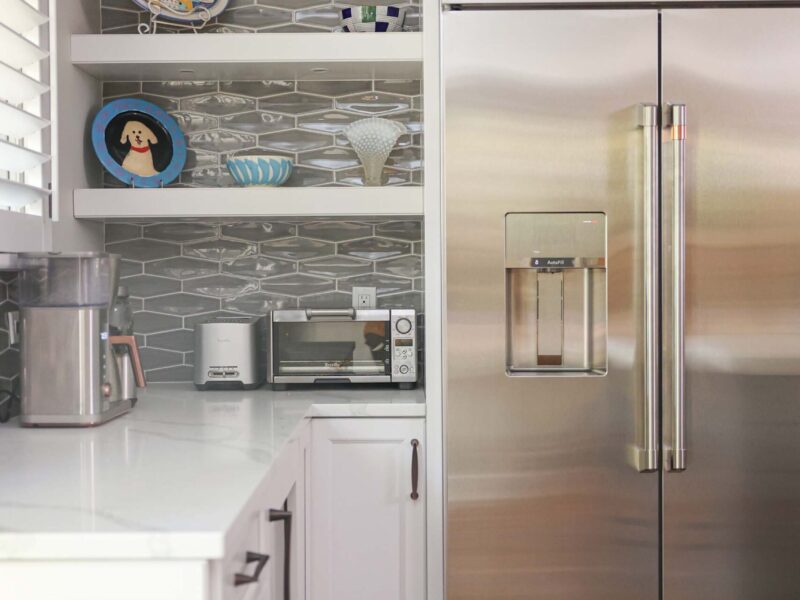Tulsa kitchen remodel featuring white cabinets, quartz countertops, floating shelves, and a decorative backsplash. The space includes a stainless steel refrigerator.
