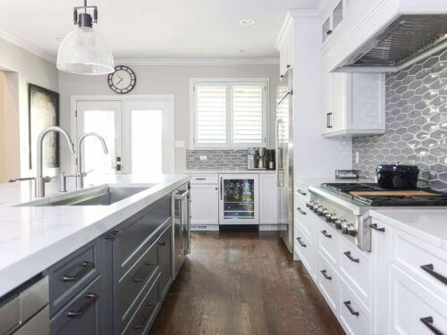 Tulsa kitchen remodel featuring gray and white cabinets, an island with a Galley Workstation, and pendant lights. The kitchen includes quartz counters, wood floors, a range top, and a tile backsplash.