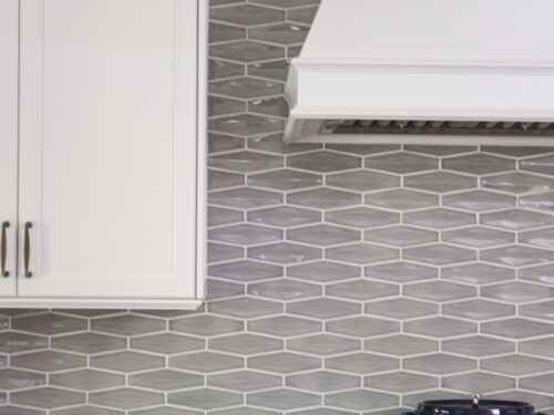 Tulsa kitchen remodel featuring a gas range top, a decorative vent hood, and white kitchen cabinets with a tile backsplash.