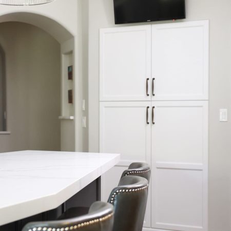 Recessed tall kitchen pantry white cabinet storage, television above, island seating Tulsa kitchen design and remodel