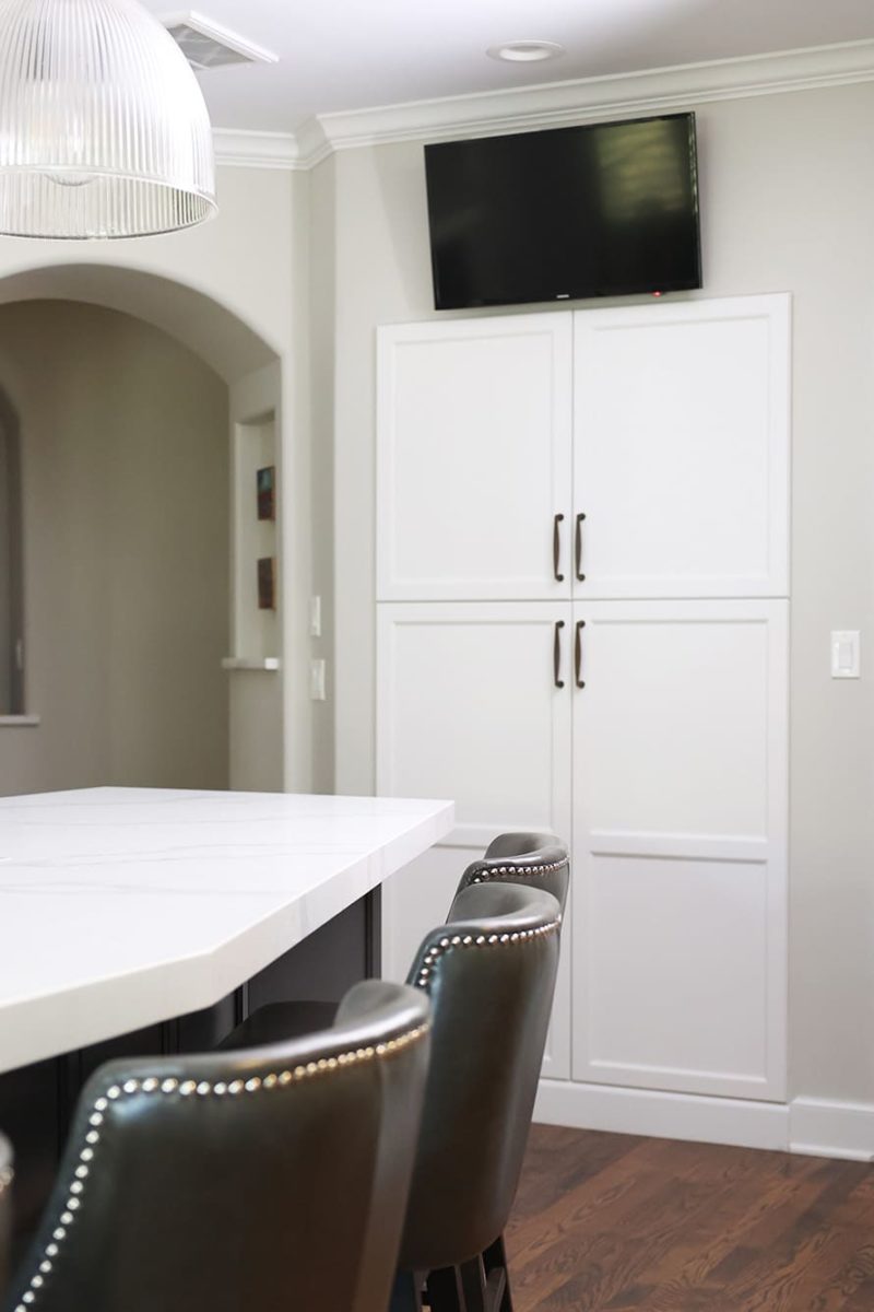 Recessed tall kitchen pantry white cabinet storage, television above, island seating Tulsa kitchen design and remodel