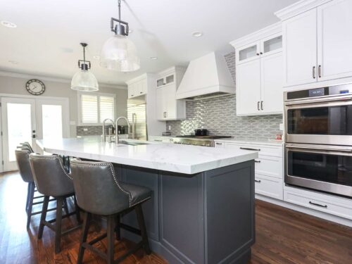Tulsa kitchen remodel featuring a Galley Workstation in the kitchen island with seating, pendant lights, and built-in double ovens. The space includes wood floors and a decorative backsplash.
