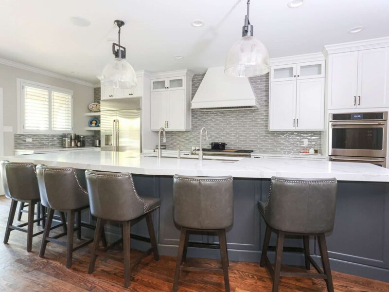 Tulsa kitchen remodel featuring "tuxedo" cabinets, a large island with seating, pendant lights, a Galley Workstation, a stainless steel refrigerator, and double ovens. The kitchen has wood floors and a decorative backsplash.