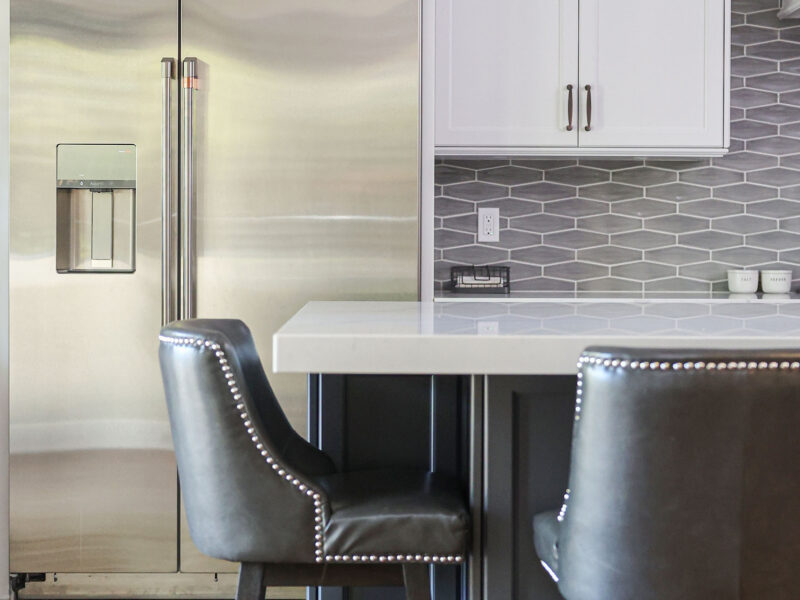 Tulsa kitchen remodel featuring two-tone cabinets, a large island with seating, stainless steel appliances, and wood floors. The design includes pendant lights and a decorative backsplash.