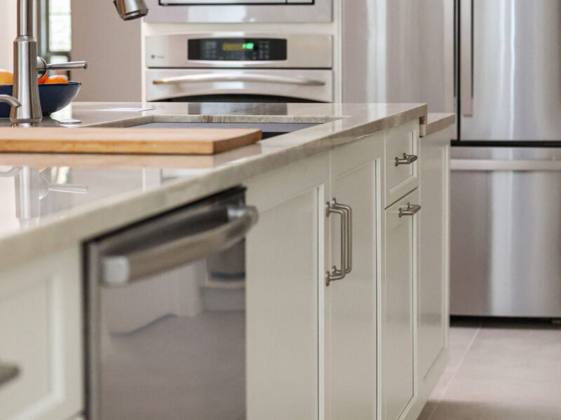 Tulsa kitchen remodel featuring a large island with a Galley Workstation and a stainless steel dishwasher. The design includes white cabinets, quartz counters, built-in ovens, and a french door refrigerator.