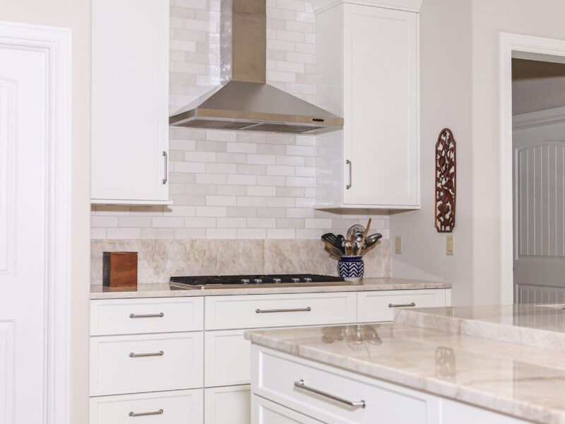 Tulsa kitchen remodel featuring an island with a gas cooktop, white cabinet storage, a vent hood, and a subway tile backsplash.