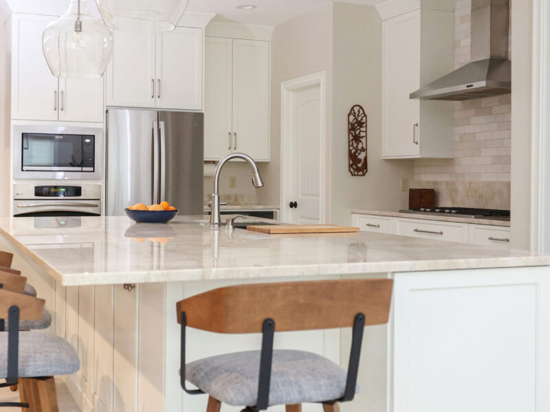 Tulsa kitchen remodel featuring a large island with a Galley sink, a built-in microwave oven, and a French door refrigerator. The design includes white cabinets and quartz countertops.