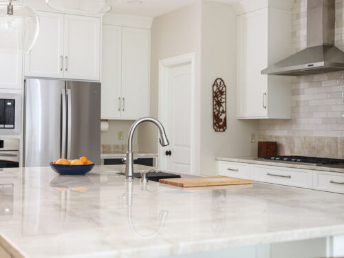 Tulsa kitchen remodel featuring a quartz countertop island with a gas cooktop, a subway tile backsplash, a vent hood, and white cabinet storage.