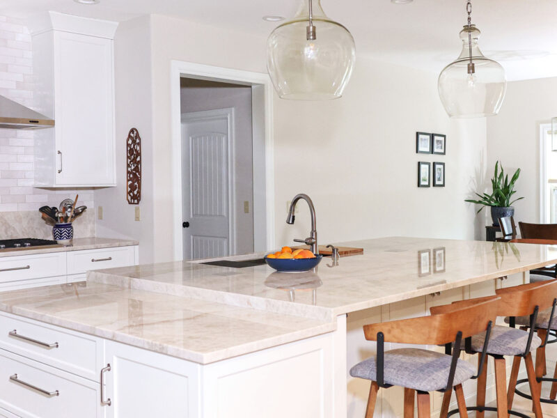 Tulsa kitchen remodel featuring white cabinets, a Galley Workstation, and a large island with a quartz counter and seating, illuminated by pendant lights.